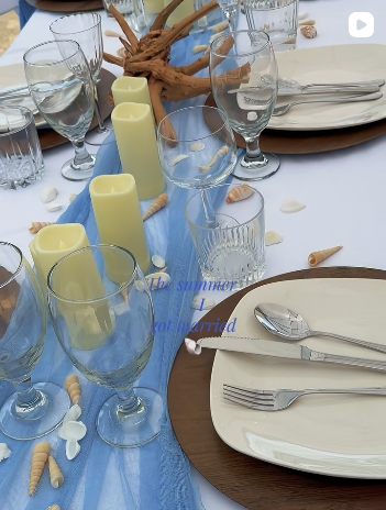 A coastal place setting with a blue gauze runner, candles, seashells and wood chargers.