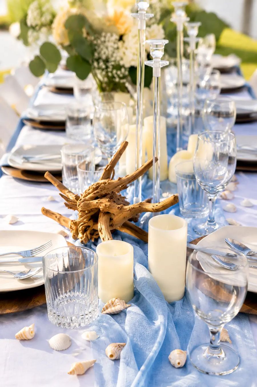 A coastal tablescape with candles, driftwood, seashells and a blue runner styled by Dreamhaus.